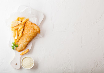 Traditional British Fish and Chips with tartar sauce on chopping board on white stone table...