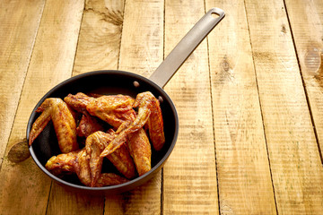 Delicious grilled chicken wings on cast-iron pan on wooden table.