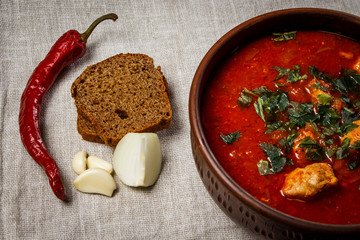 Stew in a brown clay bowl with garlic, onions, bread and pepper on sackcloth