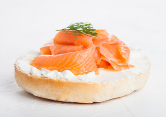 Fresh healthy bagel sandwich with salmon, ricotta and dill on light kitchen table background....