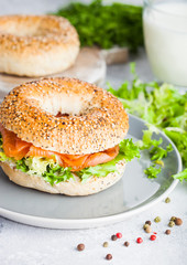 Fresh healthy bagel sandwich with salmon, ricotta and lettuce in grey plate on light kitchen table background. Healthy diet food. Glass of milk and fresh vegetables