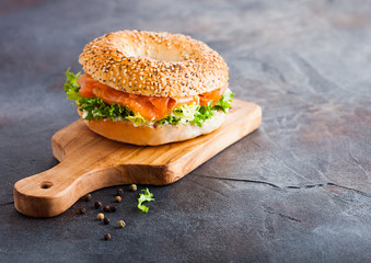 Fresh healthy bagel sandwich with salmon, ricotta and lettuce on vintage chopping board on stone kitchen table background. Healthy diet food. Space for text