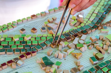 Ceramic design. Ceramic mosaic. The man organizes with a tweezers a puzzle of ceramic elements for the construction of ceramic artworks. Men's terracotta mosaic.
