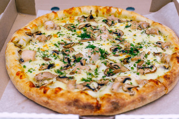 Pizza in a cardboard box on a light background. Top view. Pizza delivery. Pizza menu. Pizza on the kitchen table.
