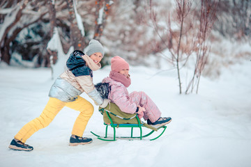 Adorable little happy girls sledding in winter snowy day.