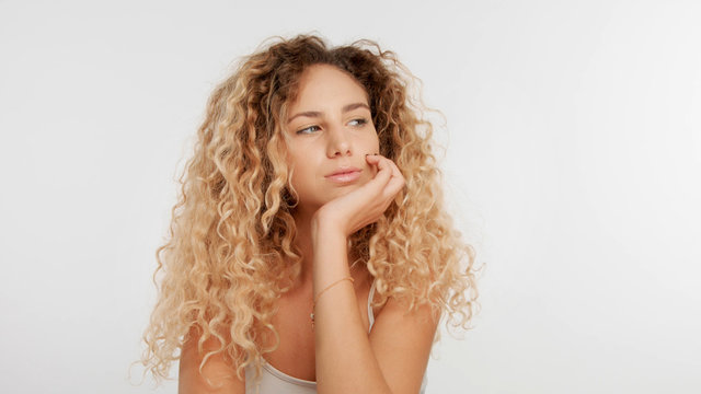 head and shoulders plan of blonde wooman with big curly hair in studio on white. Bored woman