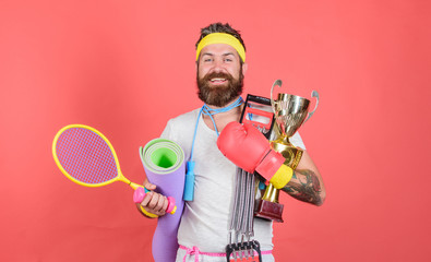 Man bearded athlete hold sport equipment jump rope fitness mat boxing glove expander racket and...