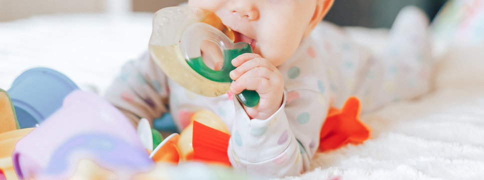 Portrait of a cute 6 month old baby, boy or girl, playing with a teething toy.