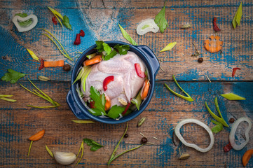 Raw chicken in a pot with vegetables on old wooden table