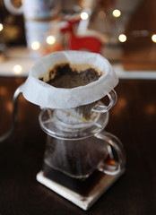 Brewing coffee with paper filter. Lights in the background