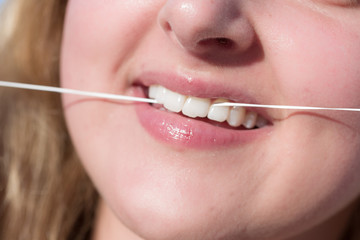Nahaufnahme eines Mundes einer jungen Frau, die Zahnseide anwendet