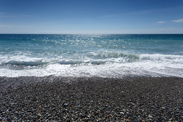 Adler, Sochi, Russia. City pebble beach. Low season, tourists are absent. Dark stones, turquoise water, blue sky