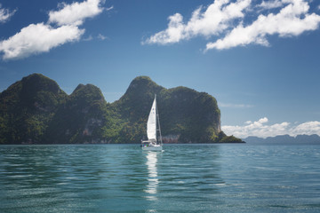 Phang Nga, Thailand. White sailing boat with tourists in the Andaman sea on a green island background. Reflection in turquoise water