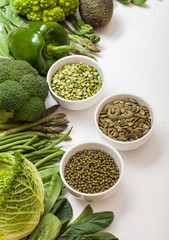 Assorted green toned raw organic vegetables on white background. Avocado, cabbage, broccoli, cauliflower and cucumber with trimmed and mung beans, pak choi, loose pepper and lettuce. Bowl with seeds