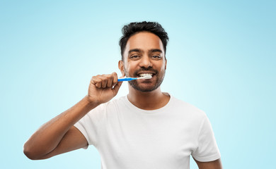 oral care, dental hygiene and people concept - smiling young indian man with toothbrush cleaning...
