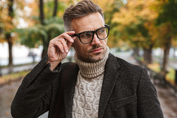 Photo of european man 30s eyeglasses, walking outdoor through autumn park