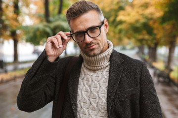 Photo of beautiful man 30s eyeglasses, walking outdoor through autumn park