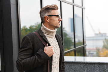 Portrait of european man 30s wearing eyeglasses, walking through city street near the building
