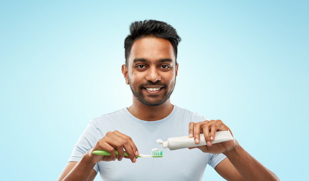 teeth cleaning, dental care and hygiene concept - smiling young indian man with toothbrush and toothpaste over blue background