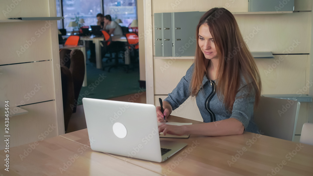Poster caucasian model sitting at the light open office. female writing notes in notebook looking in the la