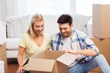 Fototapeta na wymiar mortgage, moving and real estate concept - happy couple unpacking boxes at new home