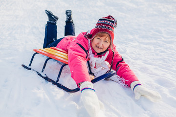 Fototapeta na wymiar Senior woman sledding down. Woman having fun lying on sleigh in winter park.