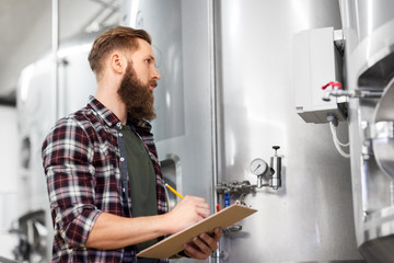 manufacture, business and people concept - man with clipboard working at craft brewery or beer plant