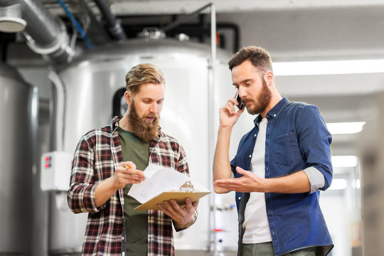 manufacture, business and people concept - men with clipboard working at craft brewery or beer plant and calling on smartphone - Powered by Adobe