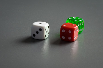 White, red and green dice with a grey background. Three dice of different color against a dark grey background.