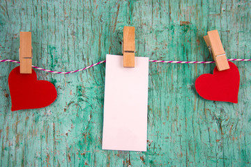 white  blank label with place for text and paper red hearts hung on clothespins on a rope on a mint green wall background