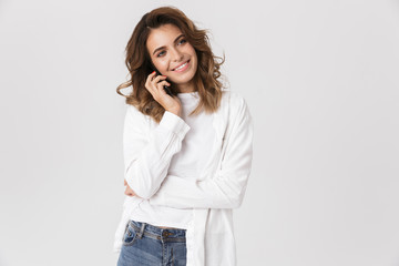 Portrait of attractive woman in casual clothes talking on mobile phone, while standing isolated over white background