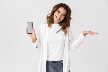 Fototapeta premium Portrait of pretty woman in casual clothes holding smartphone, while standing isolated over white background