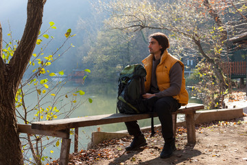 Fototapeta premium Man taking a rest on the bench by the lake while hiking in nature.