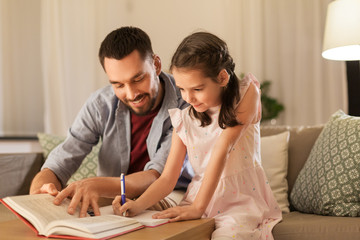 education, family and homework concept - happy father and daughter with book writing to notebook at...