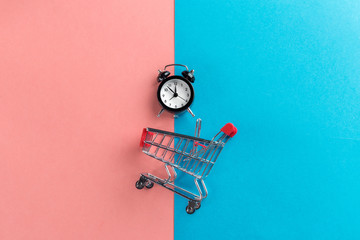 Small shopping cart with alarm clock. Shopping time concept