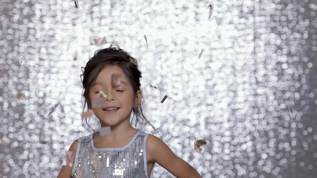 cute happy little girl child in a silver dress dancing on background of silver bokeh.