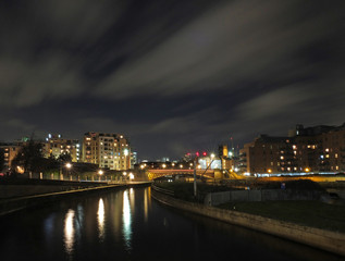 Fototapeta na wymiar panoramic cityscape view of leeds at night from the river aire with crown point bridge and apartments reflected in the water and parish church illuminated behind modern developments