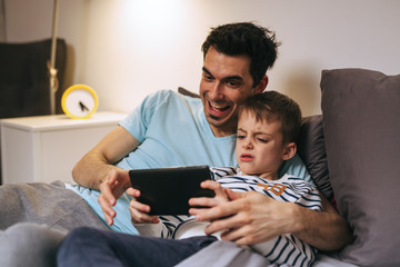 father and son playing games on tablet at home
