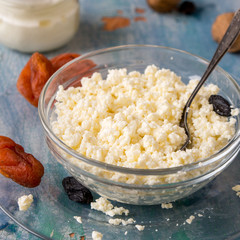 Natural and healthy food. Fresh homemade cottage cheese, a small jar of sour cream, raisins and dried apricots on an old wooden table. 