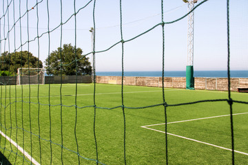 Look through net to empty football field in soccer stadium. Soccer field with green grass in football sport stadium behind net curtain. Sport equipment, football goal, white line, soccer field corner.