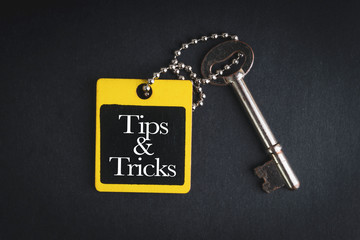 TIPS & TRICKS inscription written on wooden tag and key on black background with selective focus and crop fragment. Business and education concept