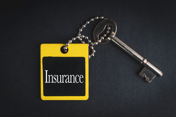 INSURANCE inscription written on wooden tag and key on black background with selective focus and crop fragment. Business and education concept