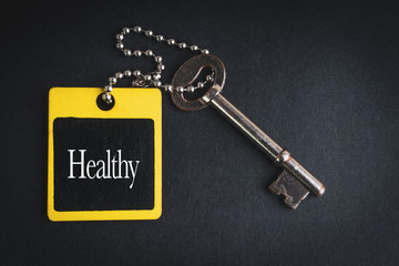 HEALTHY inscription written on wooden tag and key on black background with selective focus and crop fragment. Business and education concept