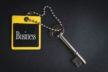 BUSINESS inscription written on wooden tag and key on black background with selective focus and crop fragment. Business and education concept
