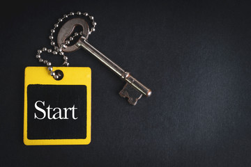 START inscription written on wooden tag and key on black background with selective focus and crop fragment. Business and education concept