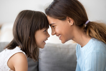 Cute little kid girl and smiling mom touching foreheads looking in eyes enjoying spending time together, happy mother and little child daughter having fun bonding playing feeling love and connection