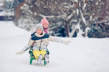 Fototapeta na wymiar Adorable little happy girls sledding in winter snowy day.