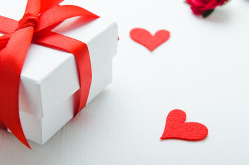 White gift box with a red bow on white background with hearts of felt. Concept congratulation on Valentine's Day, Women's Day.