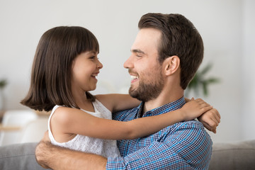 Cute funny kid girl laughing looking at father talking having fun with happy loving dad, little child daughter embracing daddy enjoying good time together, positive emotion and sincere communication