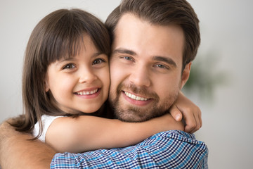 Happy little kid hugging dad holding tight cuddling looking at camera, cute child girl embracing...
